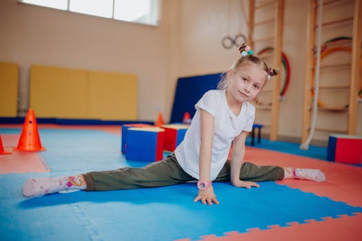 Young girl showing flexibility while practicing splits indoors on colorful mats in a playroom setting.