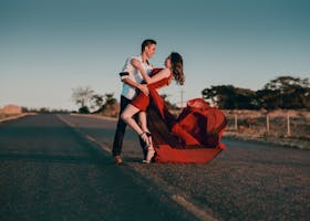 A couple in a passionate dance pose on an empty highway at sunset, showcasing love and romance.