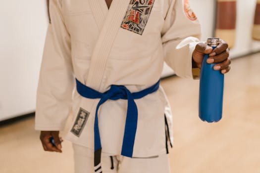 Close-up of a martial artist in a blue belt holding a water bottle indoors.